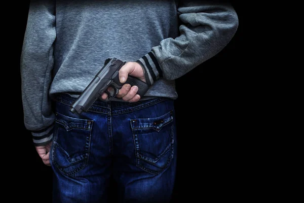 Hombre sosteniendo un arma detrás de su espalda contra un fondo negro. concepto de peligro, crimen — Foto de Stock