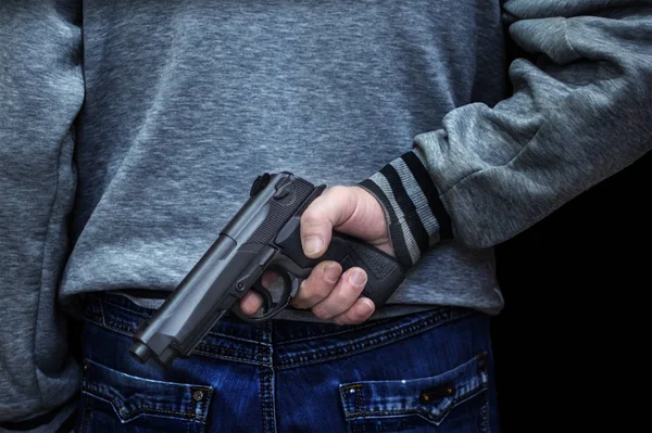 Hombre sosteniendo un arma detrás de su espalda contra un fondo negro. concepto de peligro, crimen — Foto de Stock