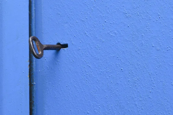 Una llave vieja en el ojo de la cerradura. Puerta de metal azul con superficie texturizada. Concepto: prohibición e inaccesibilidad, secreto, confidencialidad . — Foto de Stock
