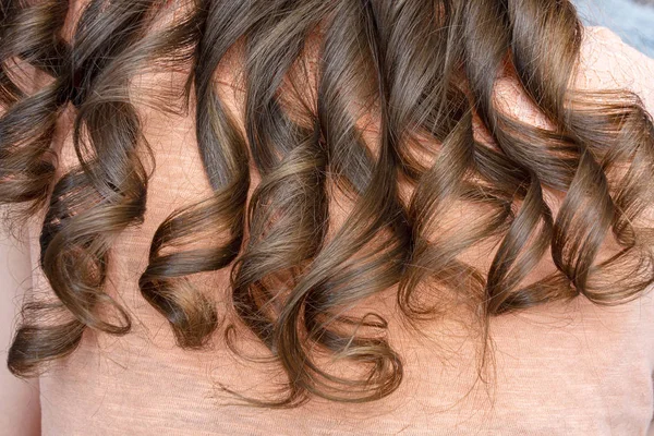 Stylista curling włosy dla kobiety brązowe włosy. Dziewczyna dba o jej fryzurę zbliżyć. — Zdjęcie stockowe
