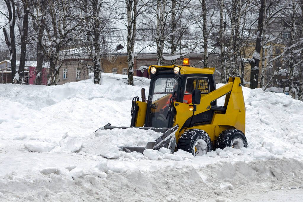 A yellow snow grader cleans snow-covered roads on a city street. concept of snowfall and rainfall. Horizontally, copy space.