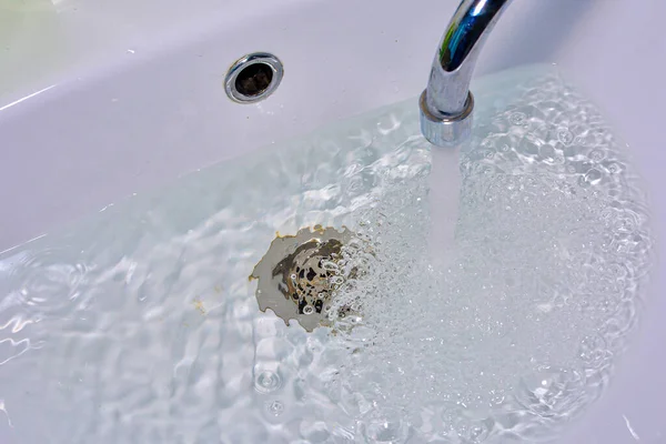 Water drains into a hole in the sink. Water supply or clogging concept.