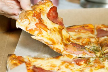 Yakın plan. Bir el taze, dilimlenmiş bir pizzayı alır. Konsept: Lezzetli yemekler, uluslararası pizza günü.