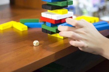 The hand dismantles the tower of multicolored wooden bars. Concept: children's leisure, board games, instability, precarious situation.