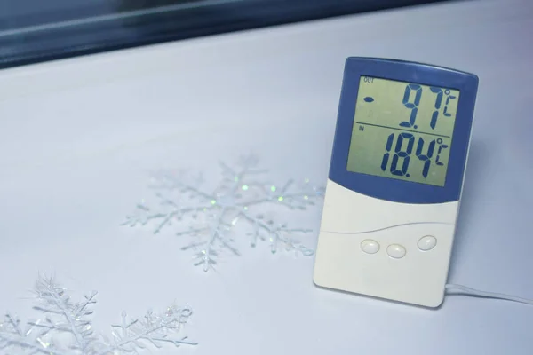 Elektroniczny termometr znajduje się na parapecie i pokazuje temperaturę w Celsjuszu na ulicy i w pomieszczeniach. Koncepcja: zmiana pogody, prognoza temperatury. — Zdjęcie stockowe