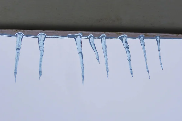 Eiszapfen an der Traufe. Konzept: Tauwetter und Frühling, die Gefahr von Eis und Eiszapfen auf dem Dach, Nachtfröste. — Stockfoto