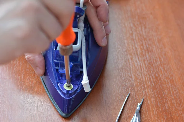 A hand with a screwdriver dismantles the iron. Concept: home appliances repair, maintenance and prevention. — 스톡 사진