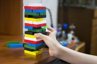 The hand dismantles the tower of multicolored wooden bars. Concept: children's leisure, board games, instability, precarious situation.
