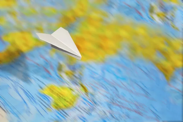 A small paper plane flies over a blurred abstract geographical m