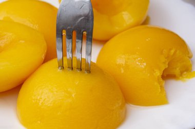 Çatalda konserve şeftali. Şeftaliler beyaz tabakta. Yakın plan..