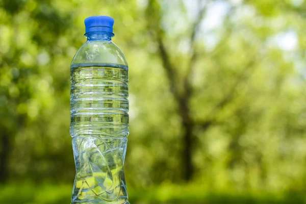 Transparent plastic bottle of fresh, natural water on the background of greenery. The concept of a healthy lifestyle, ecology and health.