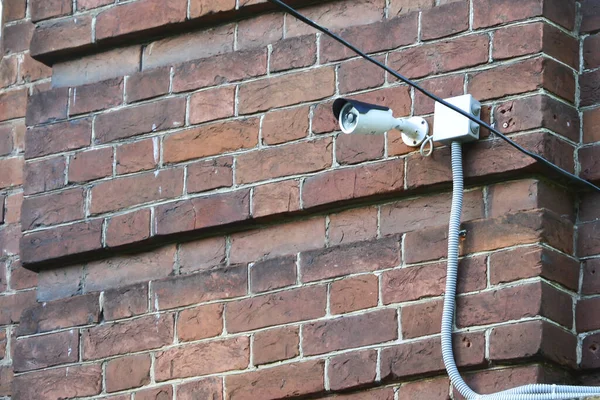 Videocamera di sorveglianza cablata montata su un muro di mattoni. Telecamera di sicurezza antifurto a filo bianco montata su un vecchio muro di mattoni . — Foto Stock