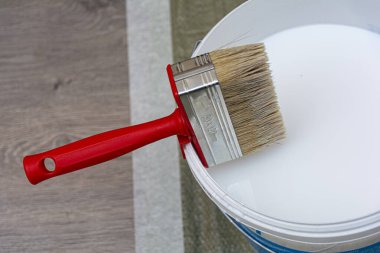 Astar ya da beyaz boyalı bir kovaya kırmızı saplı fırça. Yakın çekim, kopyalama alanı. Konsept: onarım ve iyileştirme, onarım için hazırlık.