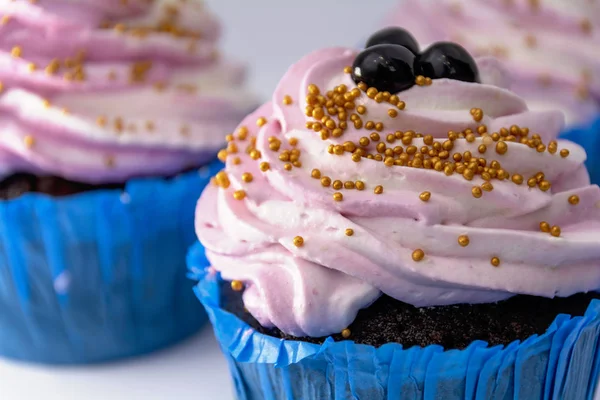 Σοκολάτα muffins σε μπλε χάρτινη μορφή με ροζ κρέμα και μούρα close-up. Αφηρημένο φόντο. — Φωτογραφία Αρχείου