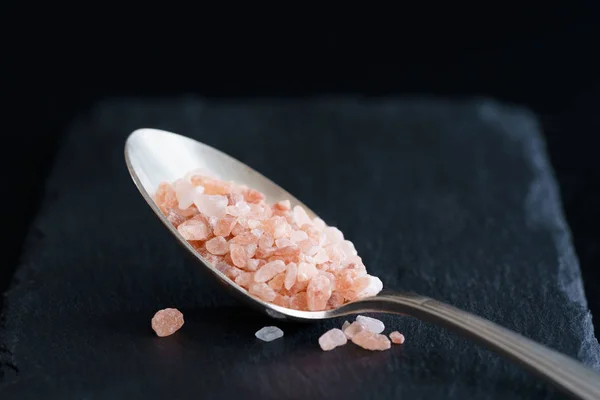 Daily salt intake, 1 teaspoon of pink Himalayan salt. Black background, high resolution, hard light