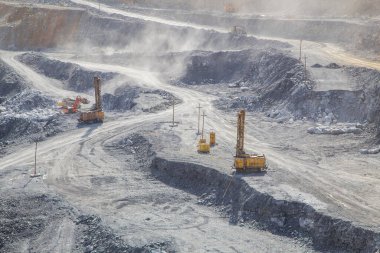 Çalışan sondaj makineleri, kazıcıları, kamyonları olan büyük bir maden ocağı.