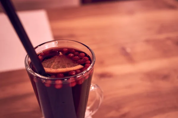 Limonlu cam bardakta sıcak şarap ve ahşap bir masada plastik pipet.                                               