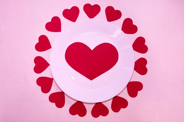 big red heart made of paper on a white plate around a lot of little red hearts for valentines day dinner                              