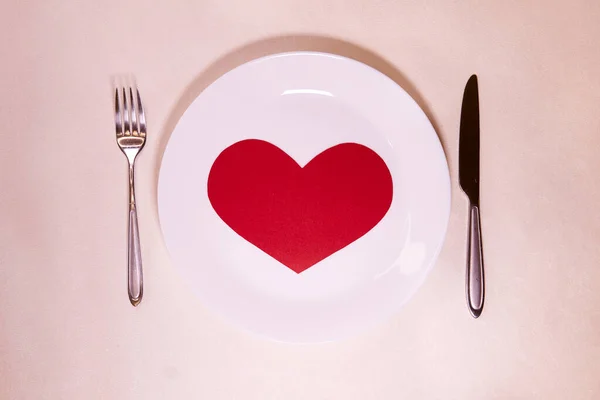 Big red heart made of paper on a white plate with a fork and knife  for valentines day                  