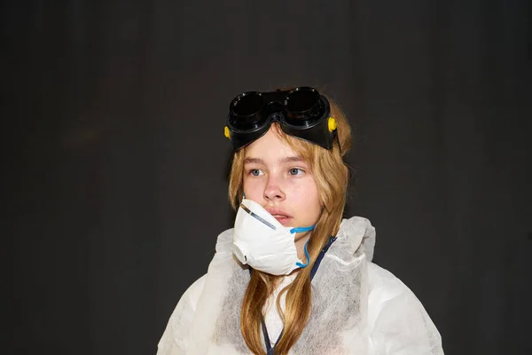 Sad girl in a medical mask and in a protective suit on a dark background
