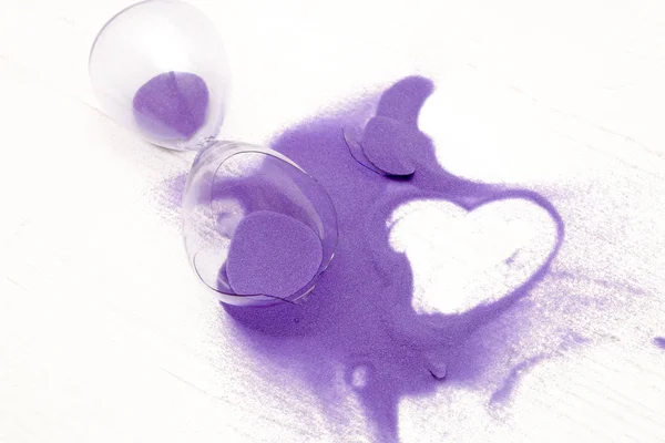 concept planting, breaking up, broken heart, broken hourglass on a white background, painted heart on purple scattered sand