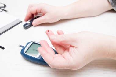 Parmağında bir damla kan olan kadın eli, kan şekerini ölçüyor, diyabet konsepti, çantanın içinde glikoz ölçer.