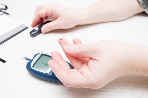 female hand with a drop of blood on a finger, measuring blood sugar, diabetes concept, glucose meter in the bac