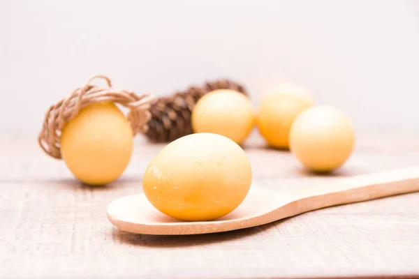 yellow egg on a wooden spoon, eggs and fir cone in blur, copy space, easter background, wooden table