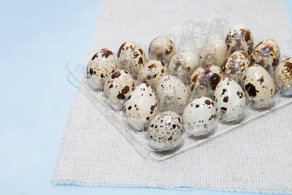 quail eggs in a transparent egg tray, light blue background, fabric, raw eggs, proper nutrition concept, close-up