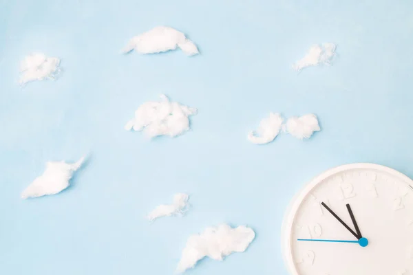 white clock on a blue background with clouds of cotton wool, the concept of time and waste, place copy