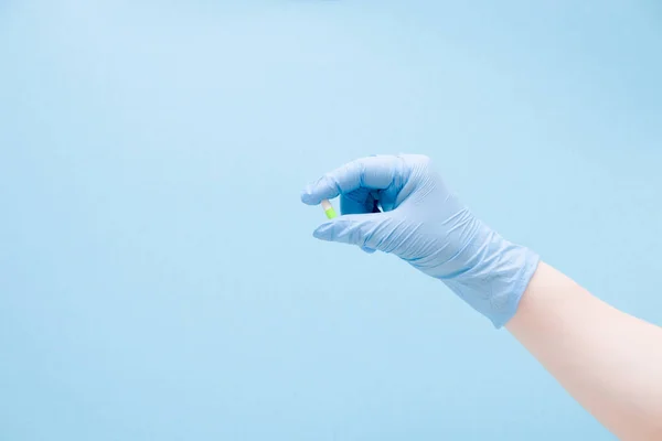 一个戴蓝色橡胶医疗手套的女性手拿着一个蓝色背景复制空间上的胶囊片 蓝色和绿色的片 治疗和保健概念 — 图库照片#