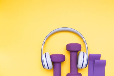 Menekşe kauçuk genişleticiler, mor dambıllar ve kulaklıklar sarı arka planda, kopya alanı, üst görünüm, evde ve spor salonunda eğitim için ekipman, sağlıklı yaşam tarzı konsepti