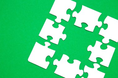 Yeşil arkaplandaki beyaz kartondan yapılma tamamlanmamış yapboz ve başka bir bulmacanın uygunsuz parçalarından biri eksik, bir parça eksik, boşluğu kopyala, uygun bir parça ara