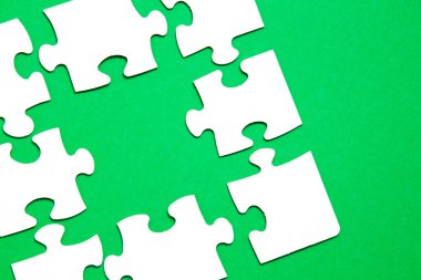 Yeşil arkaplandaki beyaz kartondan yapılma tamamlanmamış yapboz ve başka bir bulmacanın uygunsuz parçalarından biri eksik, bir parça eksik, boşluğu kopyala, uygun bir parça ara