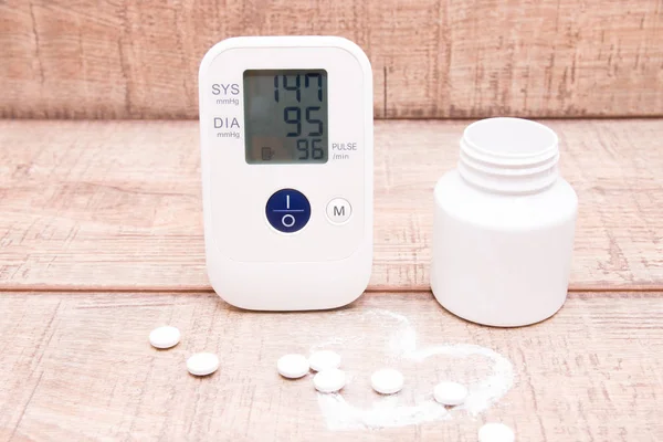 blood pressure monitor and white jar with tablets on a wooden background, heart made of white powder, pulse drawn, copy space, heart pressure concept