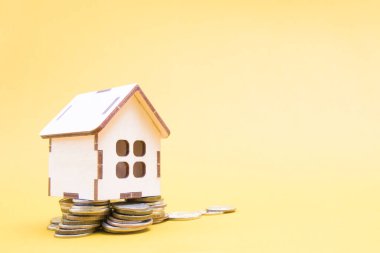 Ahşap küçük dekoratif ev bir yığın madeni para, sarı arka plan, kopyalama alanı, emlak konsepti satış ve satın alma, ev kirası, elektrik faturaları üzerinde duruyor.
