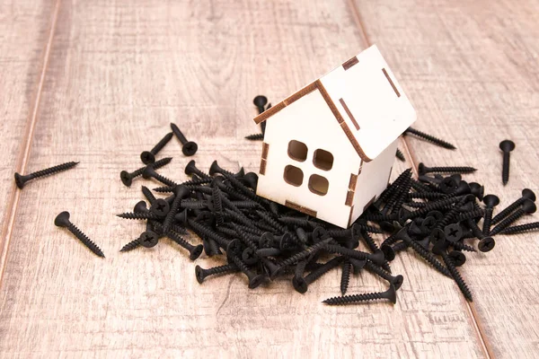 a wooden small house with a window stands on a pile of black screws, a house on nails, wooden background, copy space, construction of a private house concept