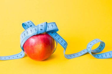 Kırmızı elma yay, kopyalama alanı, sarı arkaplan, diyet ve kilo kaybı kavramına sahip mavi bir ölçüm bandıyla bağlanmış.