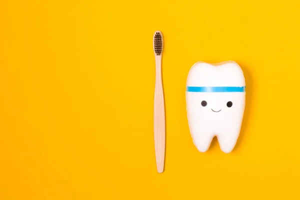 tooth model and bamboo toothbrush on yellow background, happy tooth, white healthy tooth, copy space, oral care concept