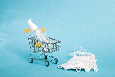 Koruyucu beyaz bebek maskeleri ve küçük bir alışveriş arabasında dezenfeksiyon jelinin yanında mavi arka plan, kopyalama alanı.