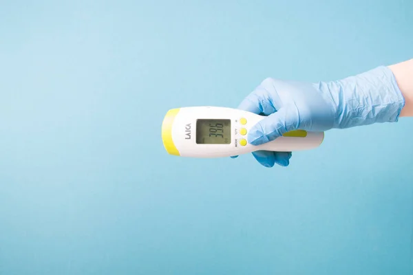 infrared non-contact temperature thermometer in hand, hand in glove, instantly measure temperature, very high temperature on a thermometer 39.6 degrees Celsius, blue background copy space