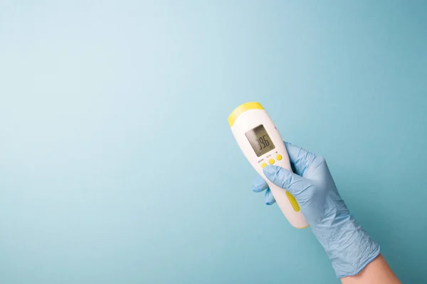 infrared non-contact temperature thermometer in hand, hand in glove, instantly measure temperature, very high temperature on a thermometer 39.6 degrees Celsius, blue background copy space