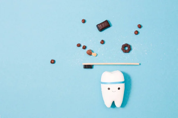 tooth model on a blue background, bamboo tooth puppy and miniature sweets, tooth decay concept, daily oral hygiene and protection against bacteria