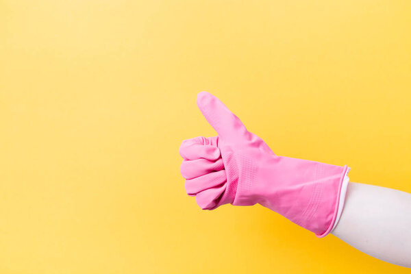 hand in a pink rubber glove for cleaning with a raised thumb up on a yellow background copy space, ok sign, approval gesture and like sign concept