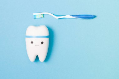 Mavi arka planda mavi kalemli mutlu diş ve plastik diş fırçası, kopya alanı, üst görünüm, ağız bakımı konsepti, diş modeli oyuncağı, pediatrik dişçilik