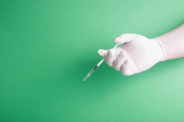 male hand in rubber white medical disposable glove holds insulin syringe green background copy space