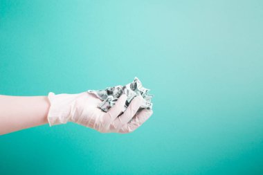 Plastik beyaz tıbbi tek kullanımlık eldiven, yeşil arka plan fotokopi alanındaki buruşmuş dolarları tutar.