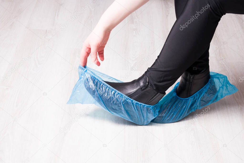 black leather boots in blue disposable shoe covers on a wooden light floor copy space, focus on boots