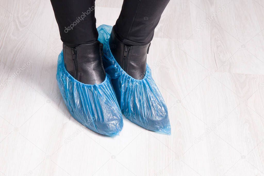 a girl stands in black leather boots with shoe covers on them, a light wooden floor, a copy space