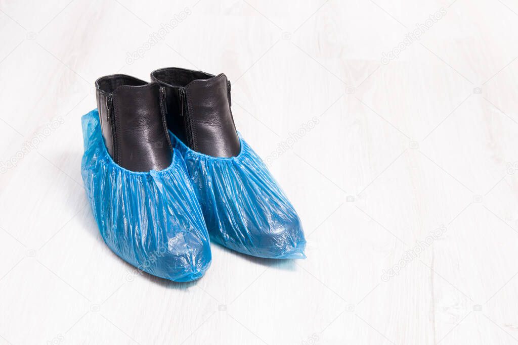 black leather boots in blue disposable shoe covers on a wooden light floor copy spac